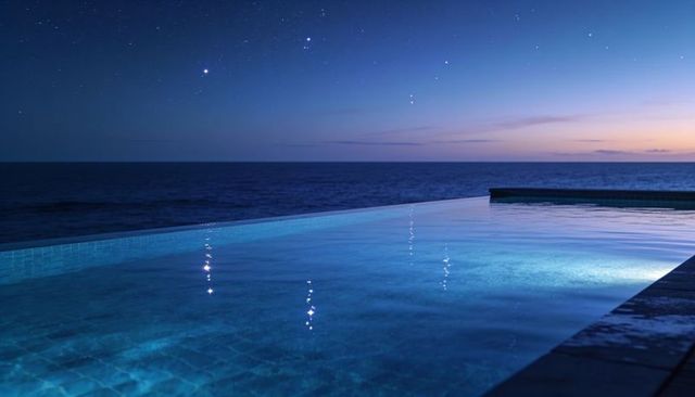 Infinity pool blending into ocean at twilight with glowing tiled edge and star reflections