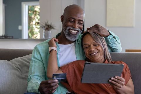 Elderly couple lounging on couch with tablet and credit card shopping online