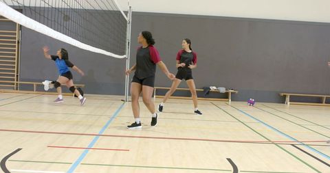 Diverse female volleyball players practicing teamwork and training on indoor gymnasium court