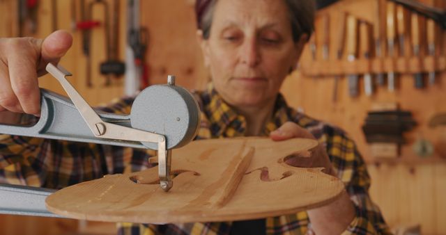 Craftsman precisely measuring violin body with caliper in woodworking workshop. Ideal for use in articles about traditional craftsmanship, handmade instruments, luthier techniques, or the importance of precision in woodworking. Can be used by websites, blogs, and magazines focused on traditional crafts, musical instruments, or woodworking.