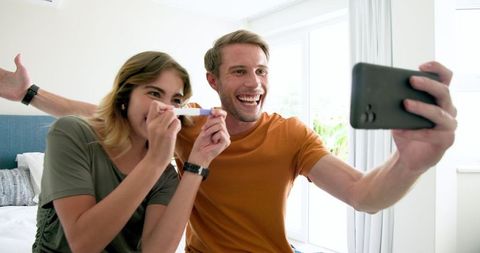 Excited couple taking selfie with positive pregnancy test