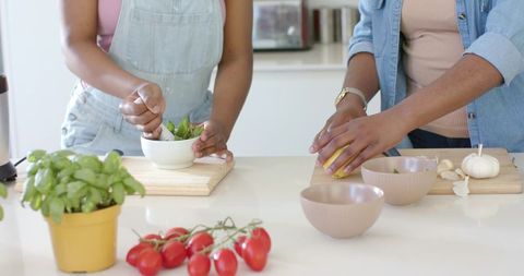 Adult and teen cooking fresh herb pesto with mortar and pestle in bright home kitchen