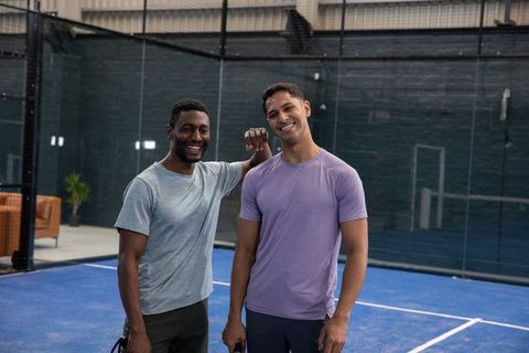 Smiling diverse male friends on indoor padel court holding rackets and relaxing