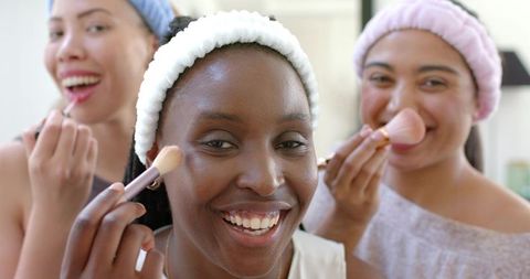 African american woman and friends applying makeup together during at-home beauty session