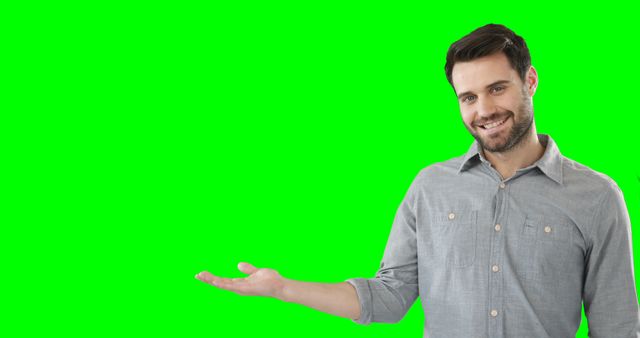 Smiling man wearing grey casual shirt, presenting blank green screen background, suitable for product or service promotion, marketing material, presentations, advertisements, or digital content creators in need of customizable backgrounds.