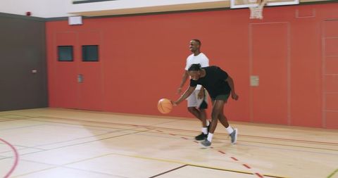 Indoor basketball one-on-one drill with teammates practicing dribbling and defense