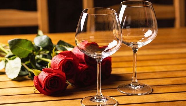 Empty wine glasses with red rose bouquet on wooden table creating romantic dinner ambience