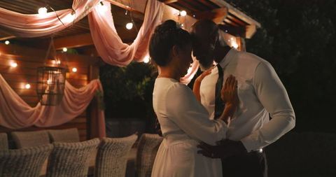 Couple dancing under string lights at intimate evening wedding celebration