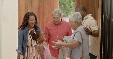 Multigenerational mixed-race family greeting grandparents at sunny open front door