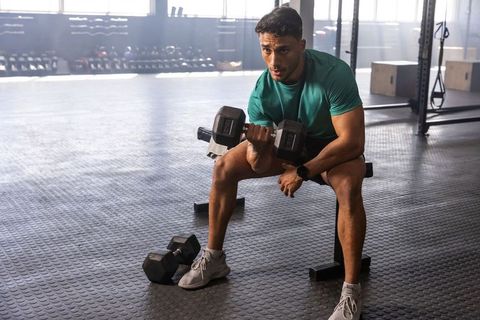 Focused man performing seated dumbbell bicep curl in gym for strength and muscle building