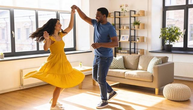 Joyful couple dancing in sunlit living room twirling yellow dress casual sneakers