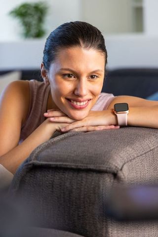 Smiling african american woman leaning on gray sofa wearing pink smartwatch