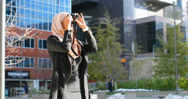 Woman in hijab standing in a cityscape, using binoculars to survey. Ideal for articles on urban exploration, diversity in cities, outdoor activities, and modern city living. Great for tourism, travel blogs, or educational materials on observing urban environments.