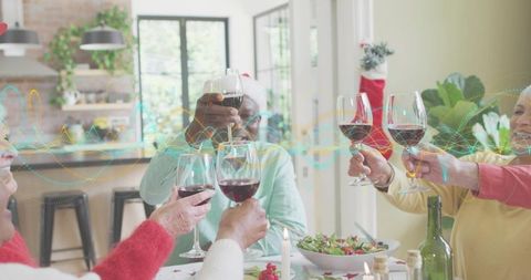 Senior Friends Toasting Red Wine at Festive Holiday Dinner with Santa Hats in Cozy Home