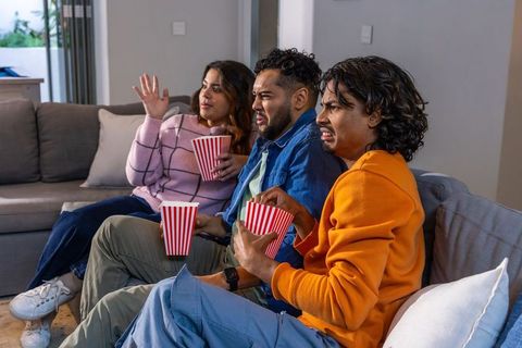 Diverse friends reacting to movie night while eating popcorn on sofa