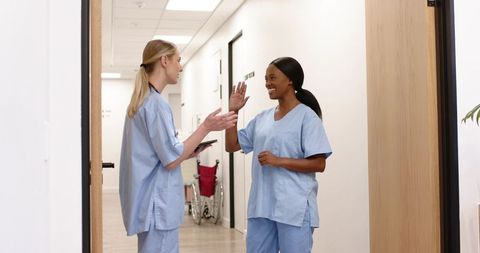 Healthcare workers exchanging high-five in clinic corridor celebrating teamwork and care
