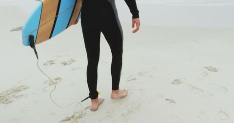 Surfer with board walking on sandy beach prepared for surfing