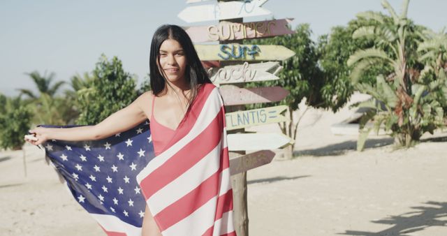 Happy hispanic woman dancing with american flag by signpost on sunny beach, slow motion. Summer, relaxation and vacations.