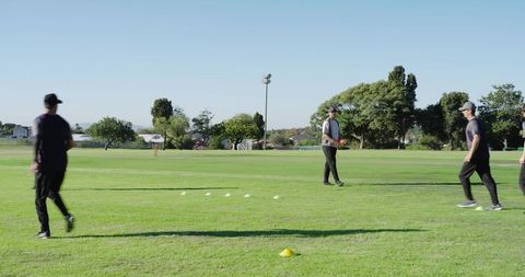 Coach nodding while athletes rotating through cone drill on grass field for agility training