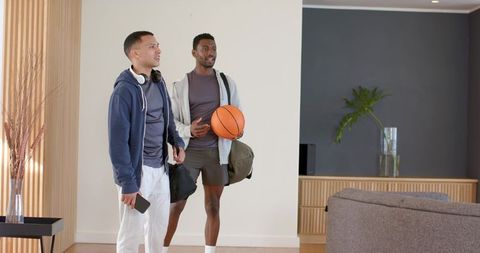 Young men returning from basketball standing in modern living room with duffel bags