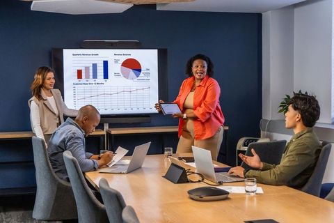 Diverse team presenting revenue charts in modern conference room using laptops and tablet