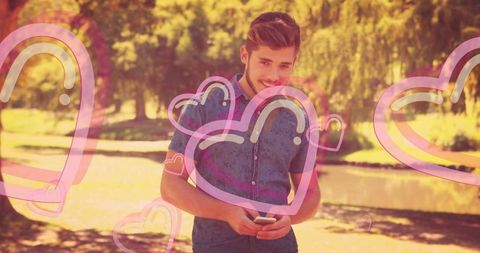 Relaxed Young Man Texting in Park with Romantic Hearts