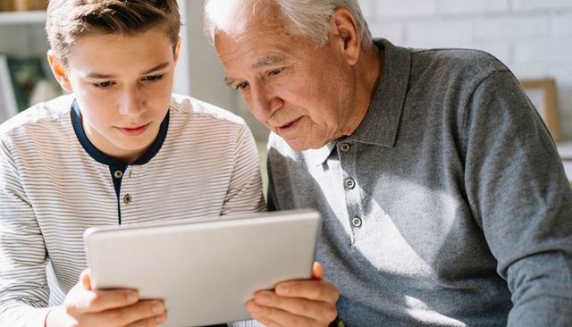Grandfather and grandson learning on tablet together in bright living room sharing technology moment