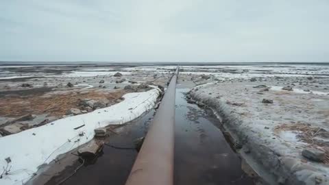 Rusty Pipeline Extending Across Desolate Snowy Marshland
