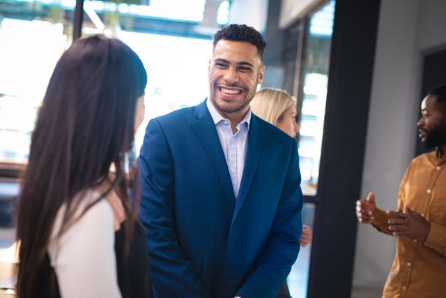 Smiling businessman engaging with diverse colleagues in a modern office environment. Ideal for use in corporate websites, business presentations, team-building materials, and professional networking content.