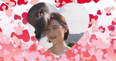 Couple pressing foreheads in heart cutout surrounded by pink hearts outdoor romance