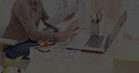 Professional Woman Utilizing Laptop and Analyzing Documents in Modern Office