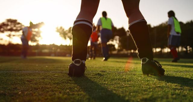 Legs of female football player playing football with team on sunny sports field. Active lifestyle, sport, competition, hobby and wellbeing, teamwork, unaltered.