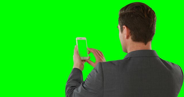 Businessman in a suit using smartphone against green screen background. Ideal for technology, business, and communication visuals. Green screen facilitates easy background removal or replacement in video and photo editing.