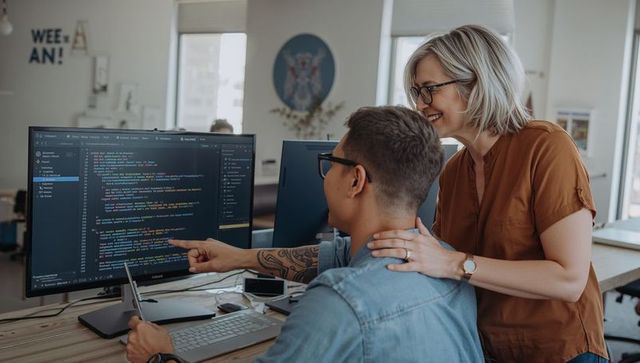 Pairing developers reviewing code on large monitor in modern open office workspace