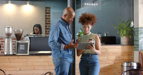 Coworkers discussing tablet at modern coffee shop counter, planning and collaborating