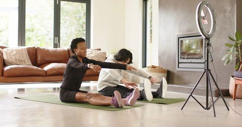 Couple stretching on mats in sunlit living room with ring light for online fitness