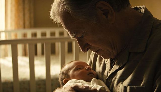 Grandfather cradling newborn in nursery showing tender care and intergenerational bond