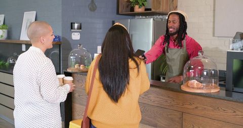 Barista scanning smartphone payment for diverse customers at cozy modern coffee counter