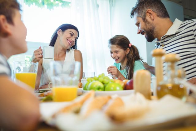 Smiling parents talking with their daughter at breakfast table in home