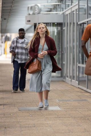 Woman walking through modern transit concourse carrying brown leather bag and phone