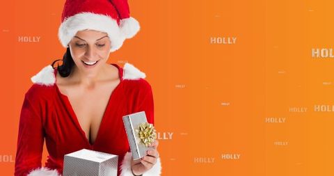 Woman in Santa Outfit Opening Christmas Gift Against Orange Background