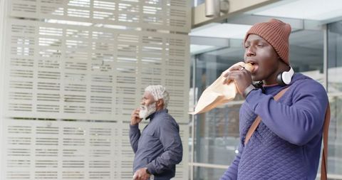 African American Men Eating Sandwiches Outside Modern Glass Office Building