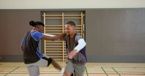 Two teammates practicing shoulder contact drill on indoor court during basketball training