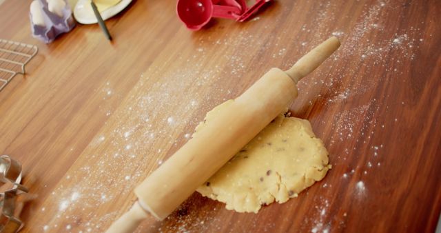 This image showcases a rolling pin pressing cookie dough on a flour-dusted wooden table. Ideal for use in food blogs, baking tutorials, recipe books, or kitchen advertisements. Highlights the messy and creative aspects of homemade baking.