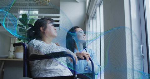 Nurse supporting senior woman in wheelchair looking out window with gentle care