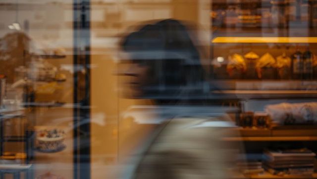 Walking blurred woman passing bakery window with pastry reflections on busy urban street