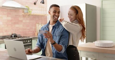 Smiling Couple in Modern Kitchen Using Laptop and Credit Card
