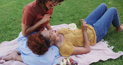 African American Women Laughing and Relaxing on Pink Picnic Blanket in Park