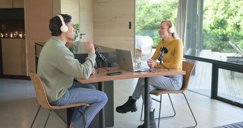 Cohosts recording podcast conversation at wooden table in bright modern home studio
