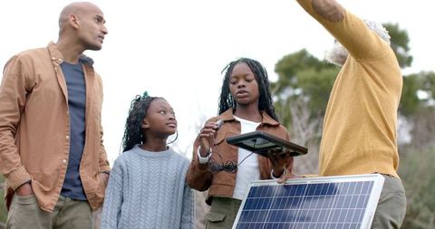 Multigenerational family learning about solar energy outdoors, children holding tablet